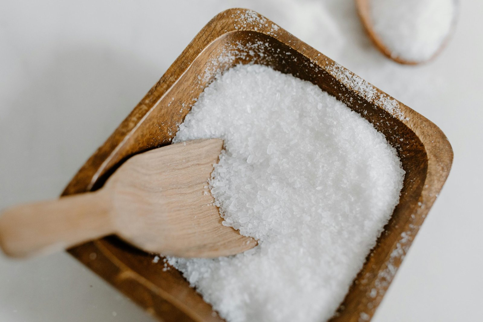 Close-up of coarse sea salt in a wooden bowl with a wooden scoop, perfect for culinary use.